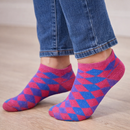 Person wearing pink and blue patterned Ankle socks with jeans on a wooden floor.