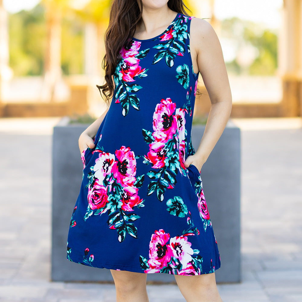 Woman wearing a blue floral dress with pink and green flowers outdoors.