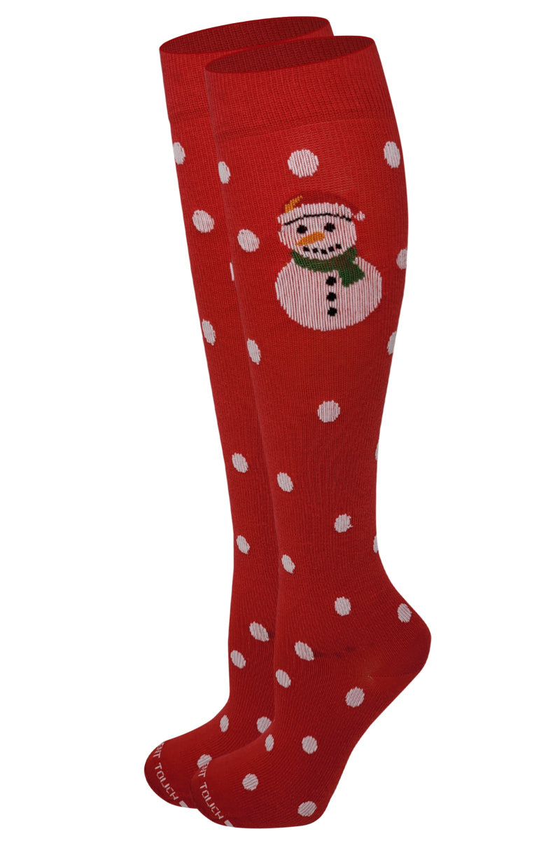 A pair of red knee-high socks with white polka dots and a Christmas design featuring a snowman.